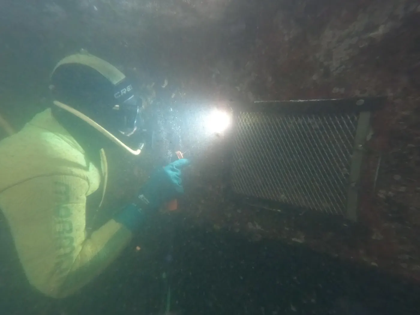 Mergulhador com lanterna inspecionando grade de estrutura submersa