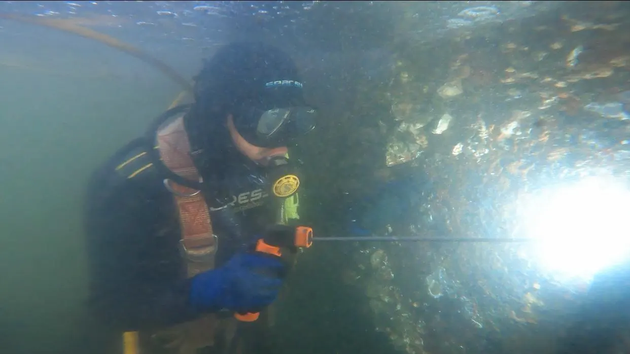 Mergulhador realizando limpeza com jato em estrutura submersa